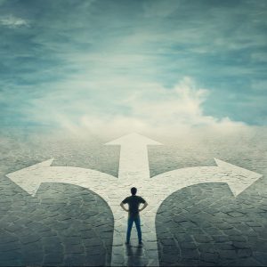 A person stands at a crossroads with three paths, contemplating a decision under a cloudy sky.