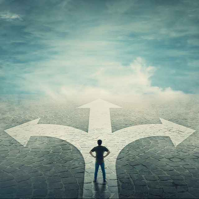 A person stands at a crossroads with three paths, contemplating a decision under a cloudy sky.