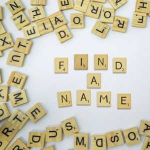 A circular arrangement of wooden letter tiles spells out 'FIND A NAME' on a white background.