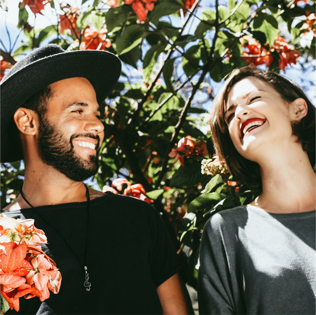 A joyful moment captured between a man and woman smiling at each other, surrounded by vibrant flowers.